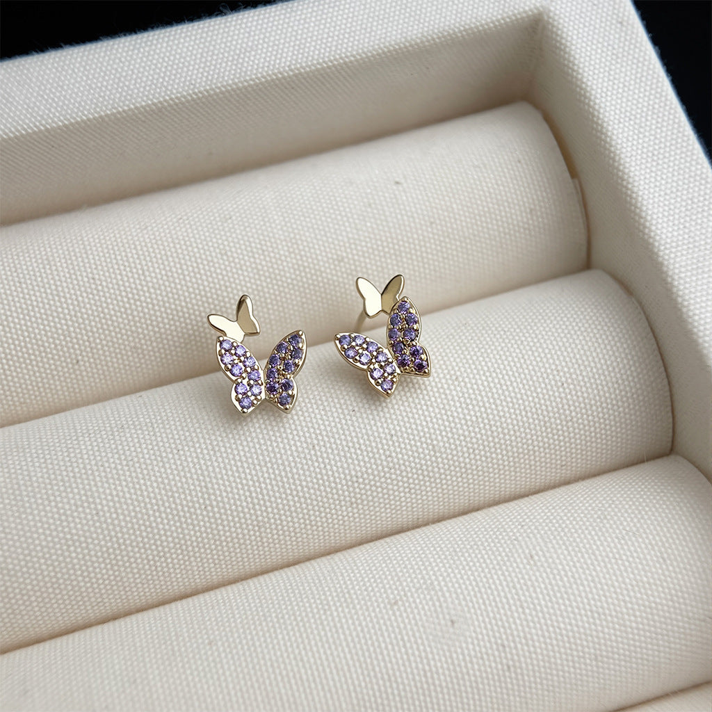 Butterfly-shaped earrings with purple gemstones on a beige jewelry display.
