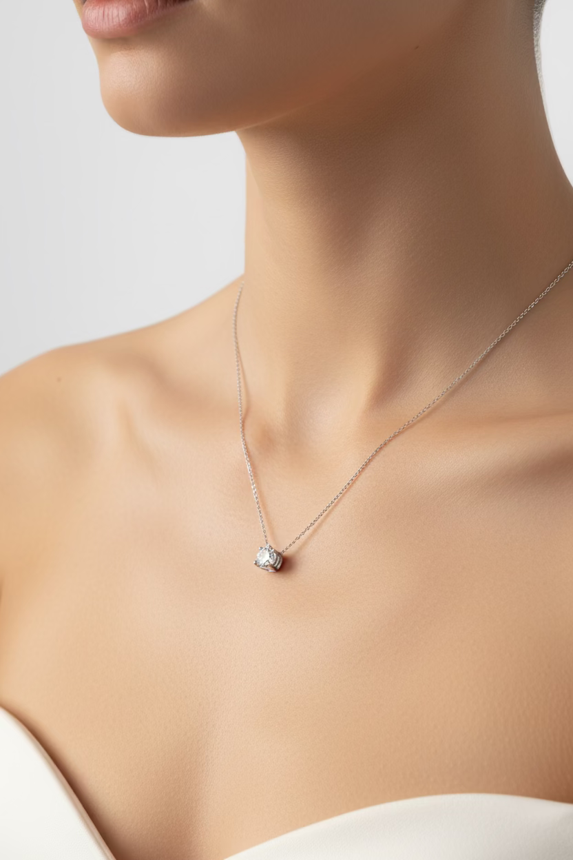 A delicate silver chain necklace with a small clear gemstone pendant, laid out on a dark gray HP laptop lid.
