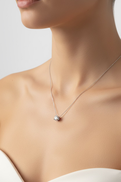 A delicate silver chain necklace with a small clear gemstone pendant, laid out on a dark gray HP laptop lid.