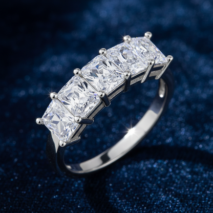 A five-stone ring featuring rectangular princess-cut clear gemstones in a silver-colored metal setting, shown on a solid black background.