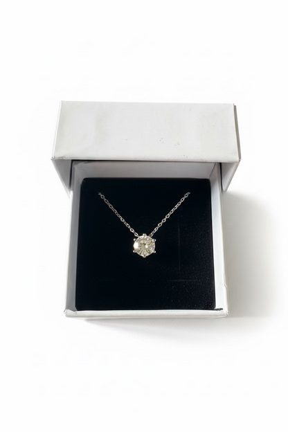A silver-toned pendant necklace with a clear faceted gemstone displayed inside an open white jewelry box with a black velvet insert