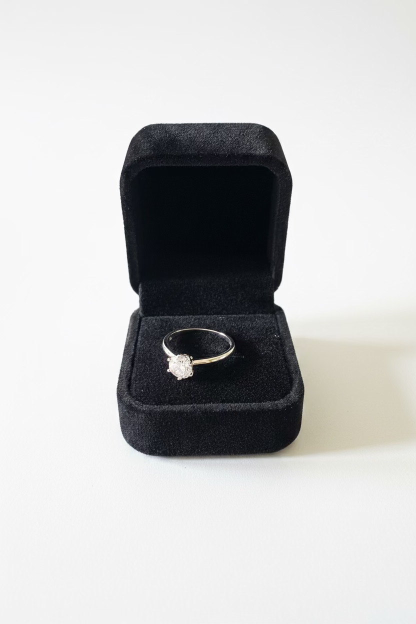A silver-toned ring with a clear center stone displayed in an open black velvet ring box 