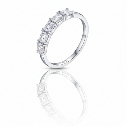 A silver band ring featuring a row of clear rectangular baguette-cut gemstones, shown on a clean white background with a soft reflection below.