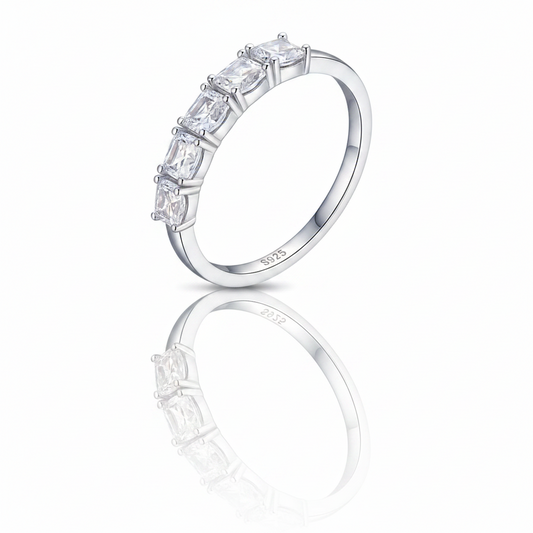 A silver band ring featuring a row of clear rectangular baguette-cut gemstones, shown on a clean white background with a soft reflection below.
