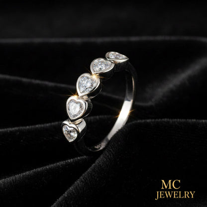 A silver band ring featuring five heart-shaped clear gemstones set in silver, displayed on a black velvet background with an MC Jewelry logo in the bottom right corner.