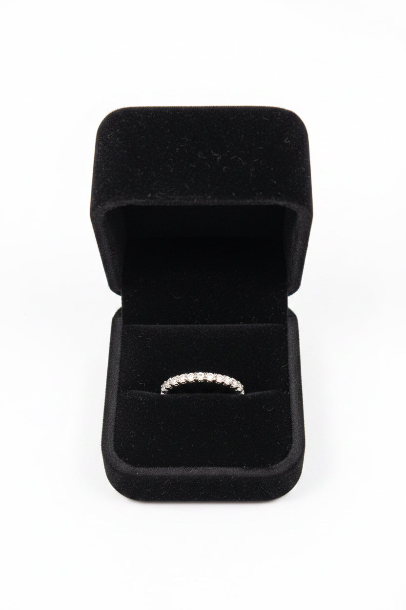 A silver band ring with a row of small clear stones, displayed inside an open black velvet ring box on a white background.