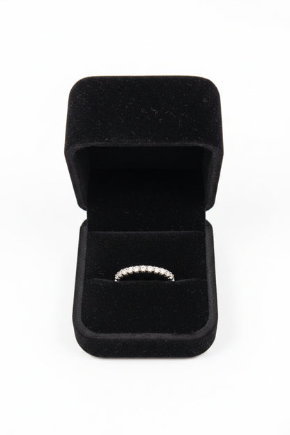 A silver band ring with a row of small clear stones, displayed inside an open black velvet ring box on a white background.