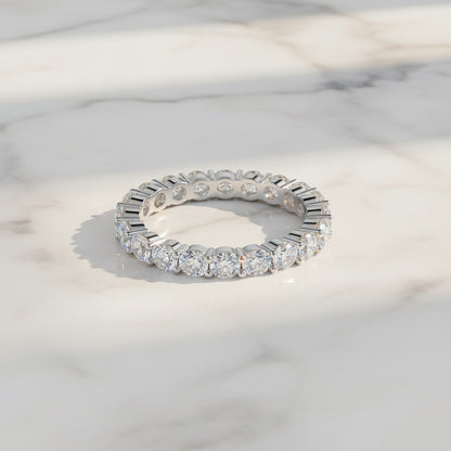 A silver diamond eternity band ring resting on a white marble surface with soft shadows.