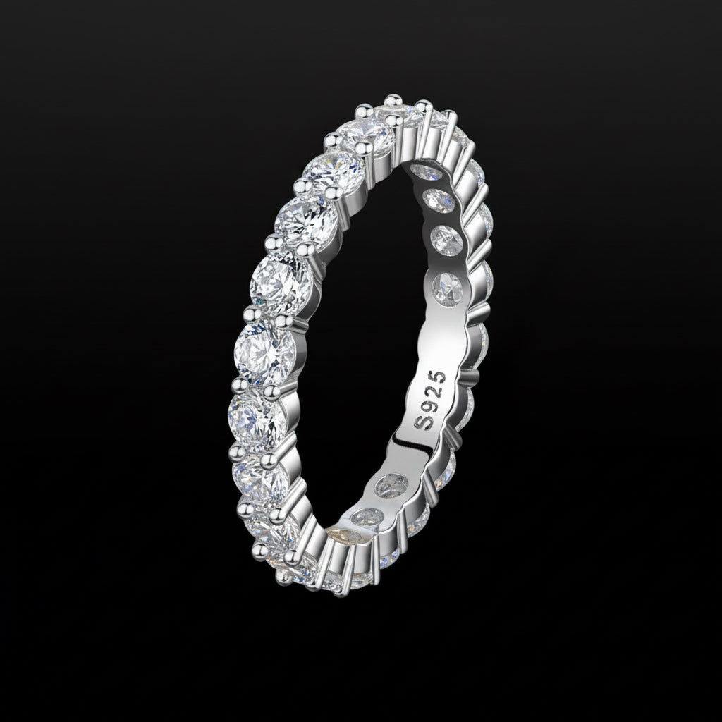 A silver eternity ring featuring round brilliant-cut diamonds set in a continuous band, shown on a solid black background. The inner band is engraved with 'S925' indicating sterling silver.