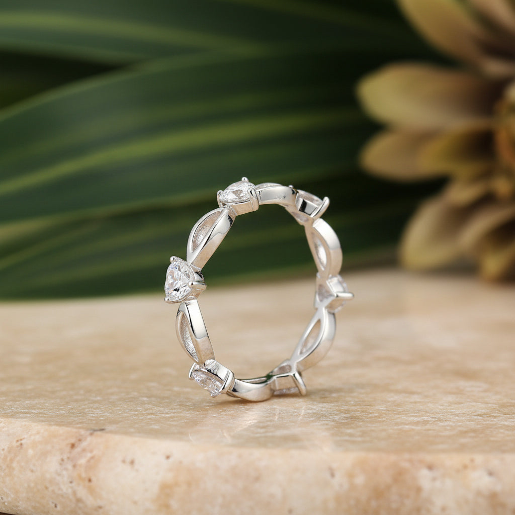 A silver infinity-style ring featuring four clear heart-shaped and oval gemstones, shown on a clean white background with a soft shadow.