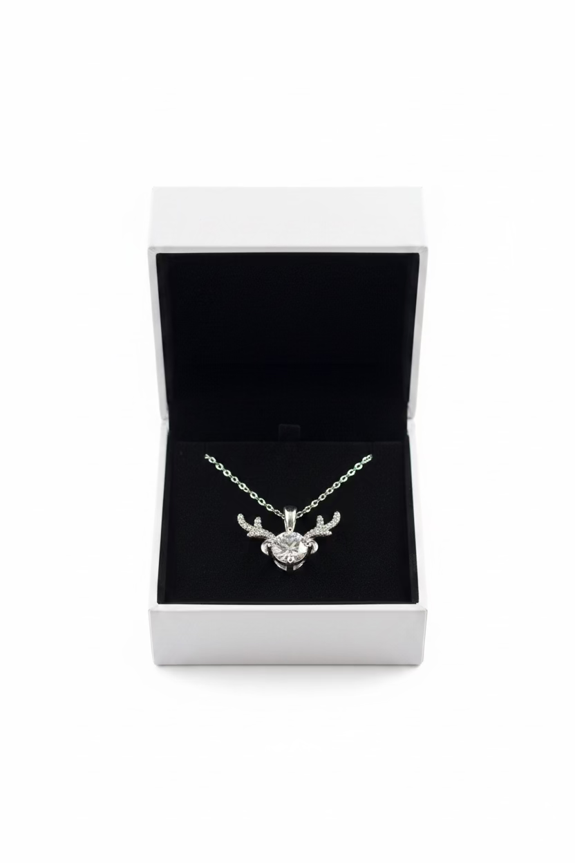 A silver pendant necklace with a reindeer head design and a central clear gemstone, displayed inside an open white jewelry box 