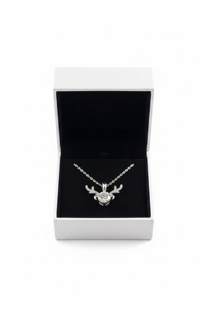 A silver pendant necklace with a reindeer head design and a central clear gemstone, displayed inside an open white jewelry box 