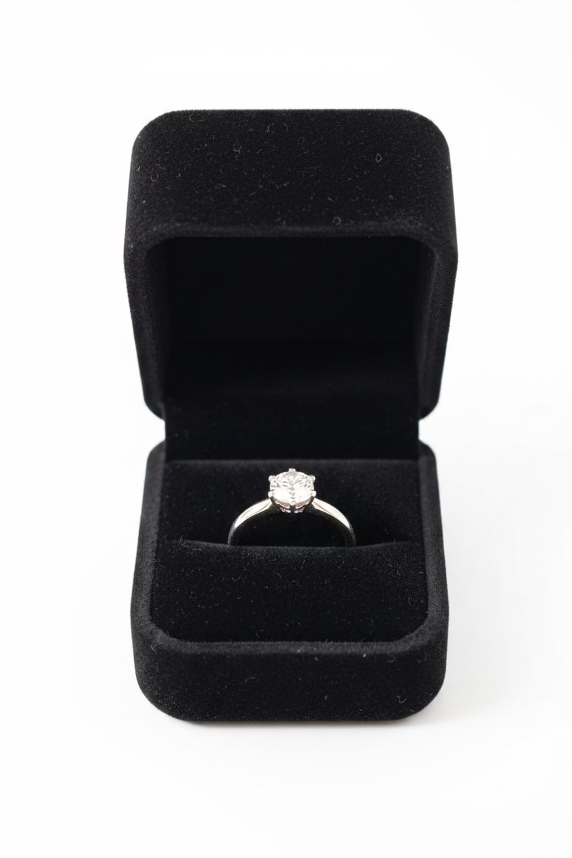 A silver ring with a small clear gemstone set in a black velvet ring box, photographed 