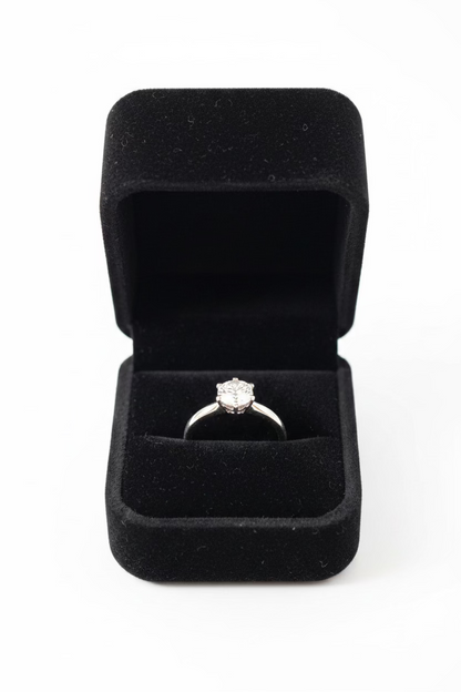 A silver ring with a small clear gemstone set in a black velvet ring box, photographed 