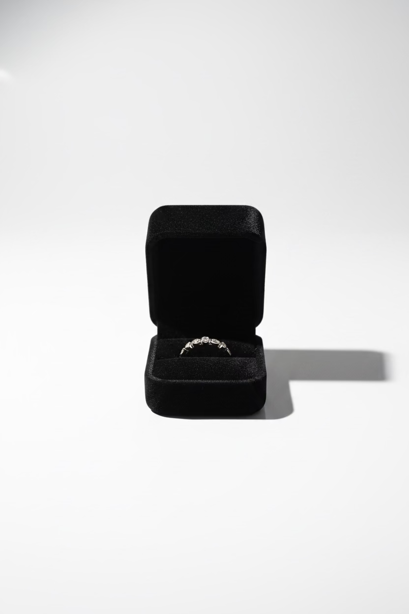 A thin gold band ring with a small central clear gemstone, displayed inside an open black velvet ring box 