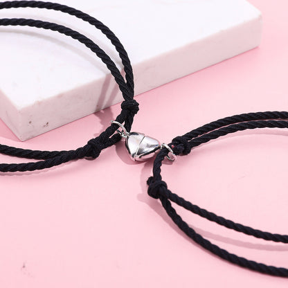 Black cord necklace with a silver heart-shaped clasp on a pink surface