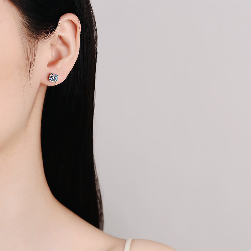 Close-up of a person wearing a silver earring with a blue gemstone on a neutral background