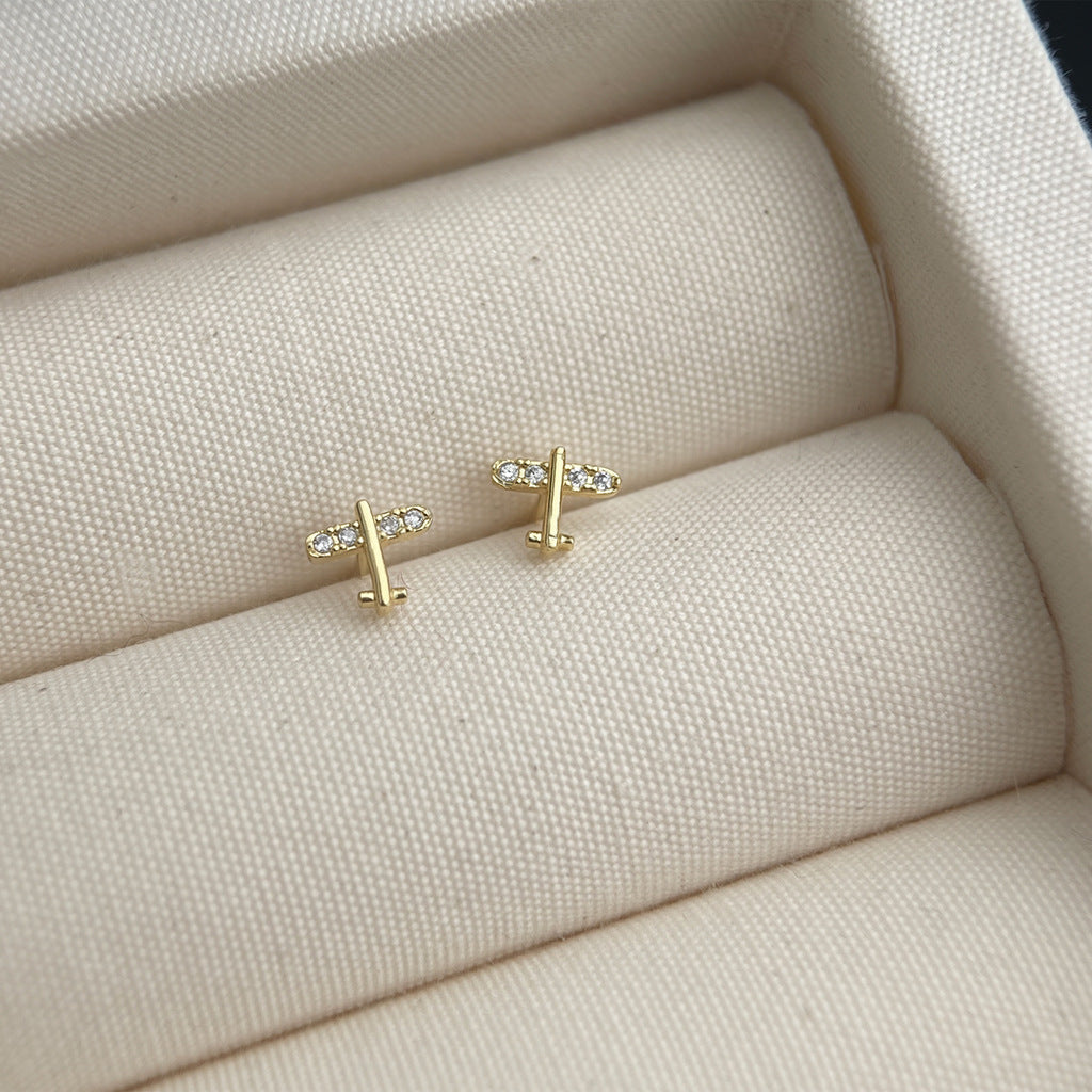Gold airplane-shaped earrings on a textured beige surface