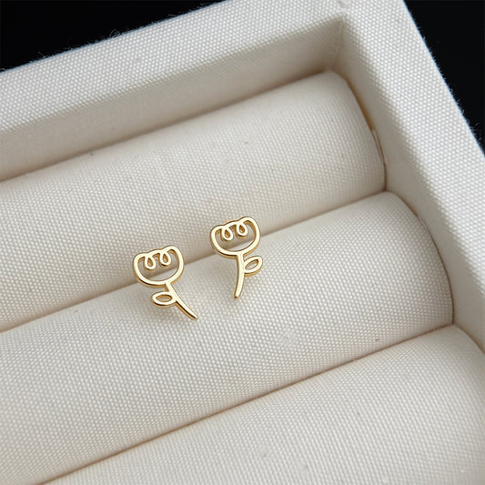 Gold rose-shaped earrings on a white fabric surface