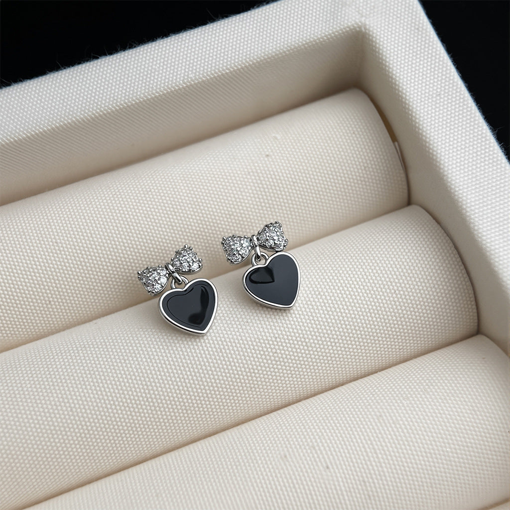 Heart-shaped earrings with black centers and silver bows on a white jewelry box.