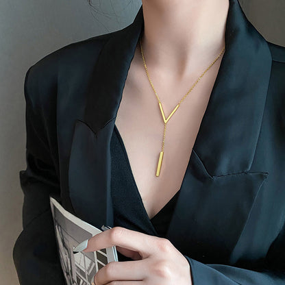 Person wearing a gold necklace with a V-shaped pendant against a dark background