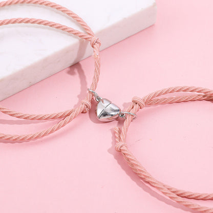 Pink braided bracelet with a silver heart charm on a pink background
