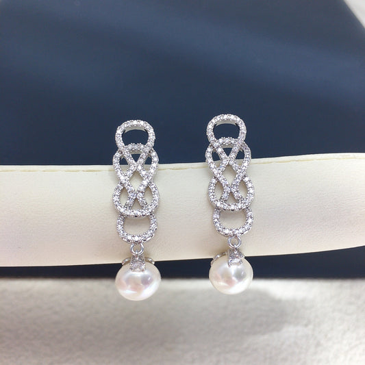 Silver earrings with intricate designs and pearl drops on a dark background